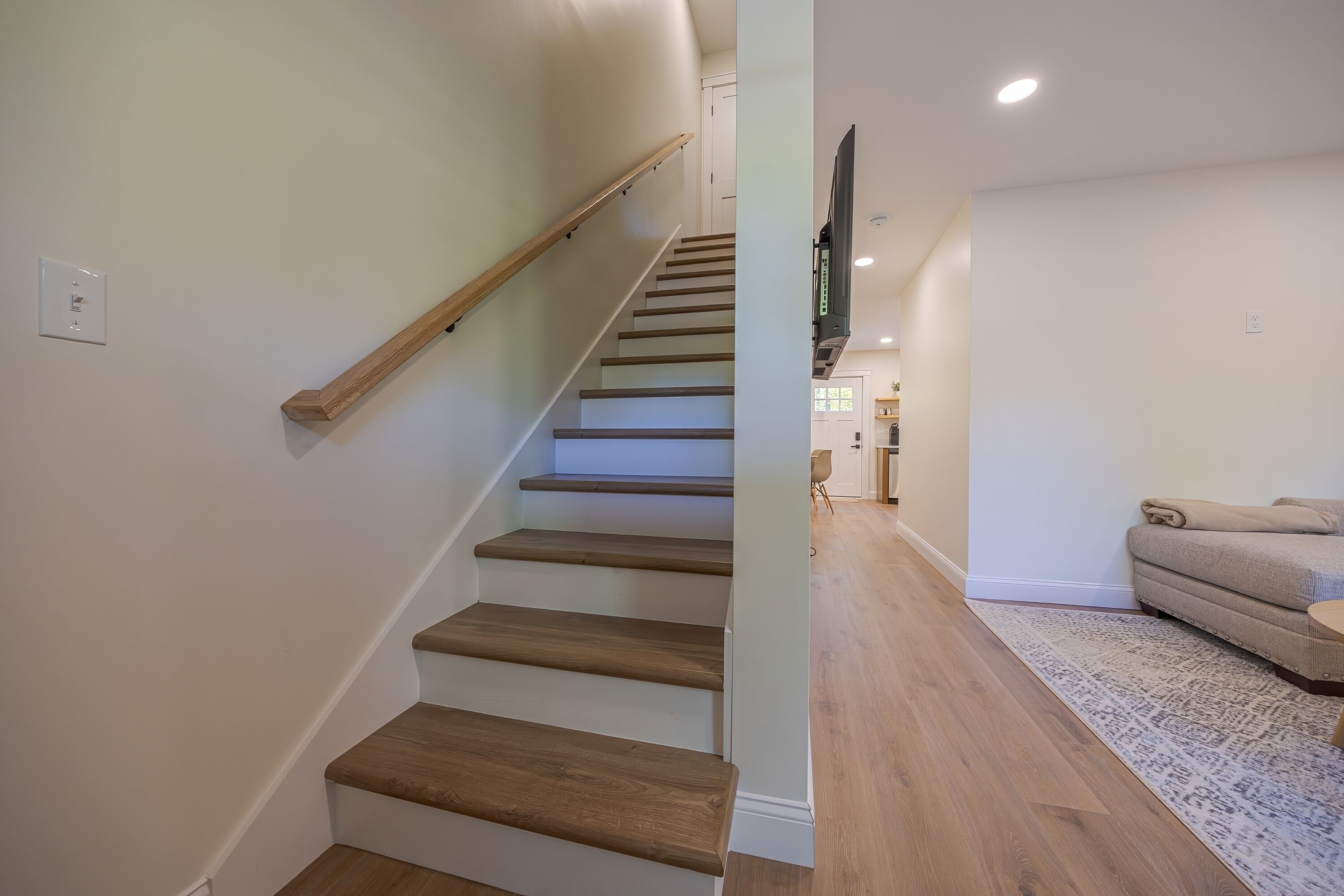 Una escalera de madera con barandilla que conduce a una sala de estar con un sofá y un tapete.