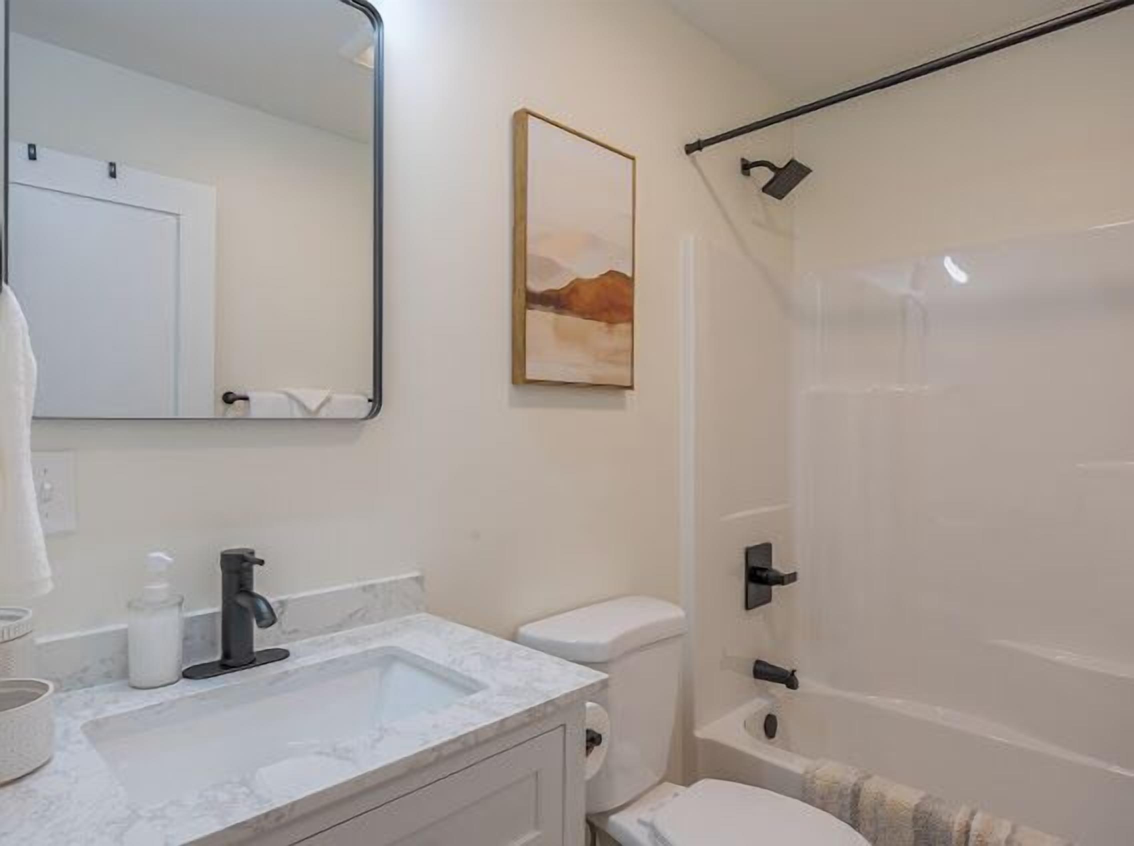 A bathroom with a white sink, mirror, toilet, and shower.