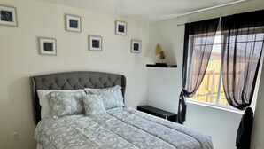 Ein Schlafzimmer mit einem großen Bett, einem Nachttisch, einem Fenster mit Vorhängen und gerahmten Bildern an der Wand.