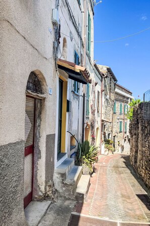 A narrow street with buildings featuring stone facades, arched doorways, and green shutters. - La casa di Bibi by Interhome (Costarainera)