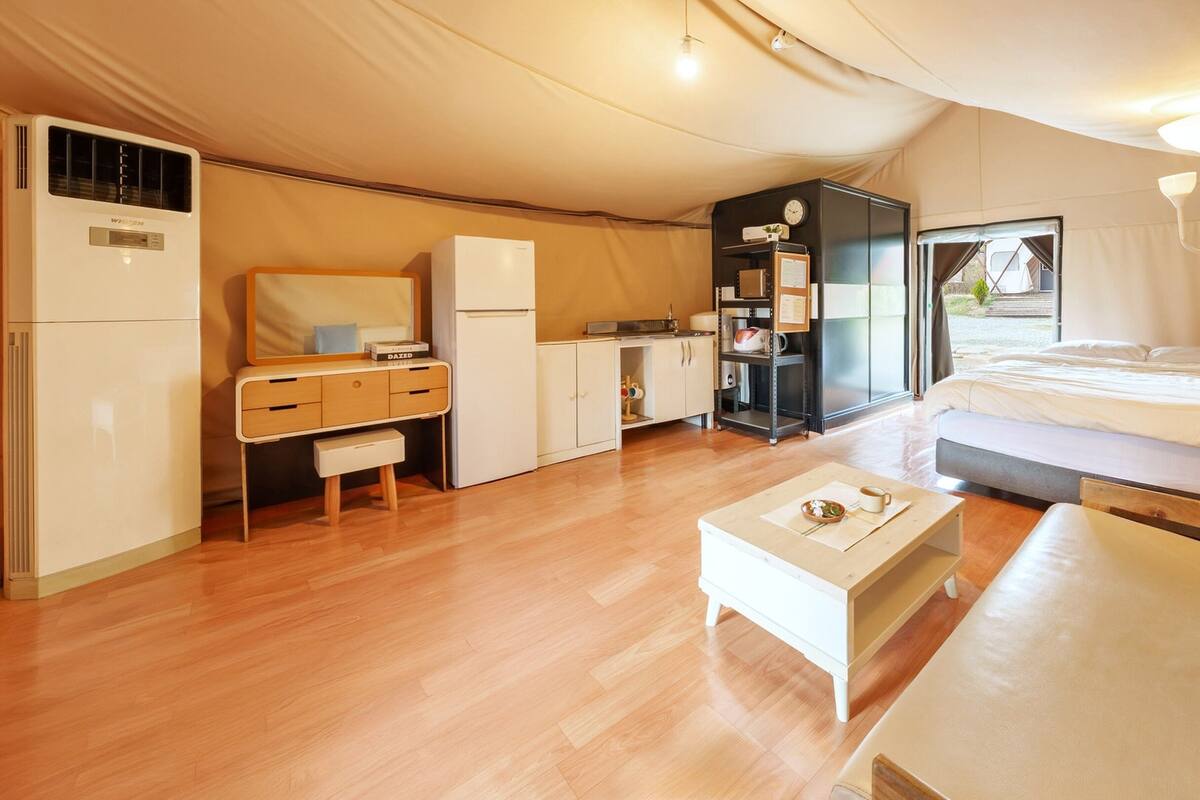 Une pièce de taille réduite, aménagée comme une tente, bien éclairée et comprenant un lit, une petite kitchenette, un bureau et un coin salon.