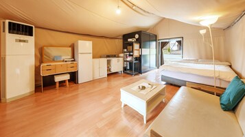 Habitación tipo tienda de campaña, compacta y bien iluminada, con una cama, kitchenette pequeña, escritorio y zona de estar.