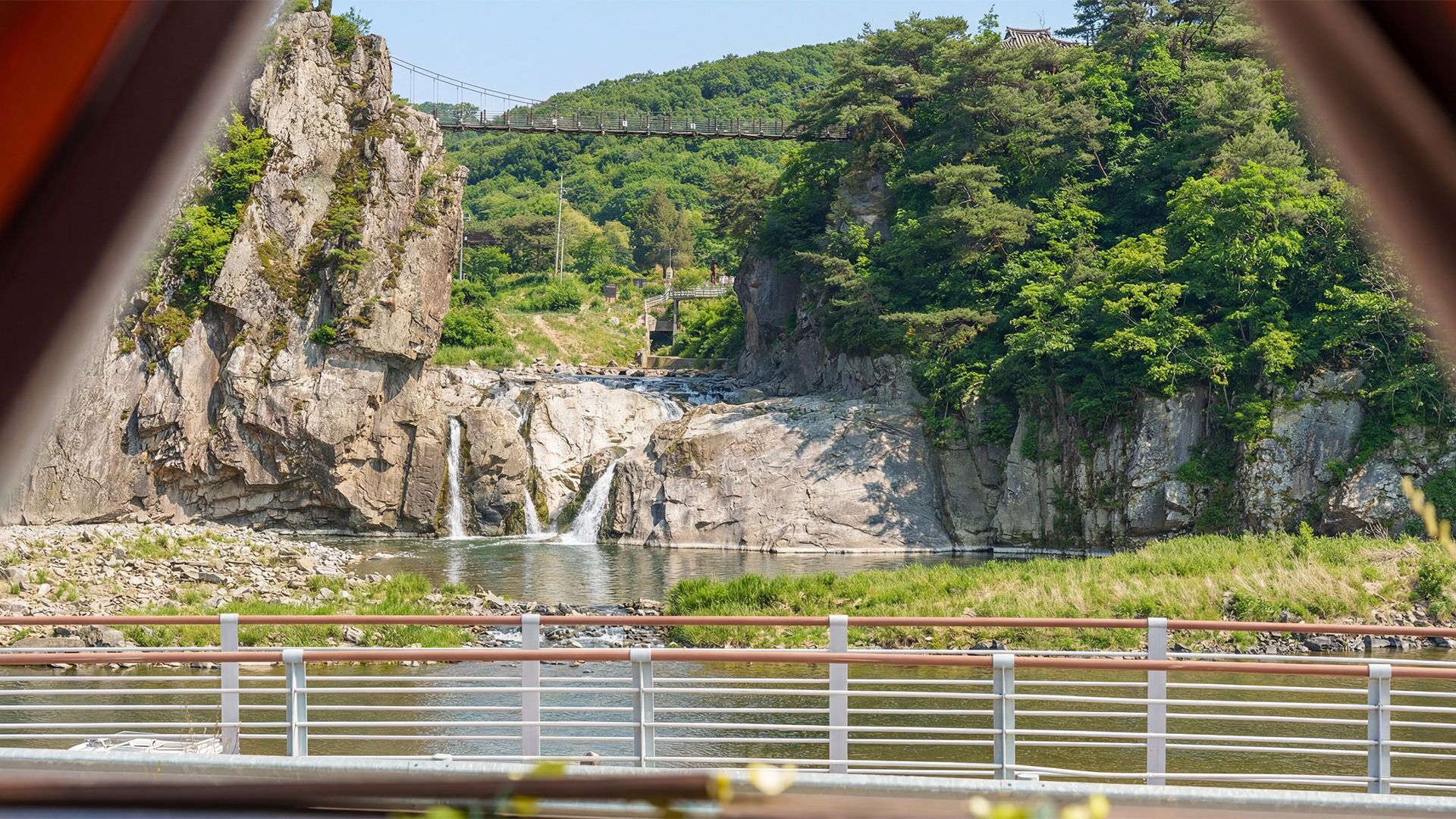 A river with a waterfall, a bridge, and a forested hillside.