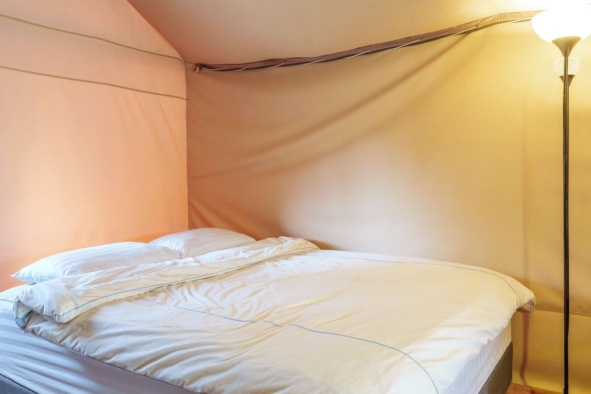 Un lit avec une literie blanche, dans une pièce aux murs de couleur pêche et dotée d’un lampadaire.