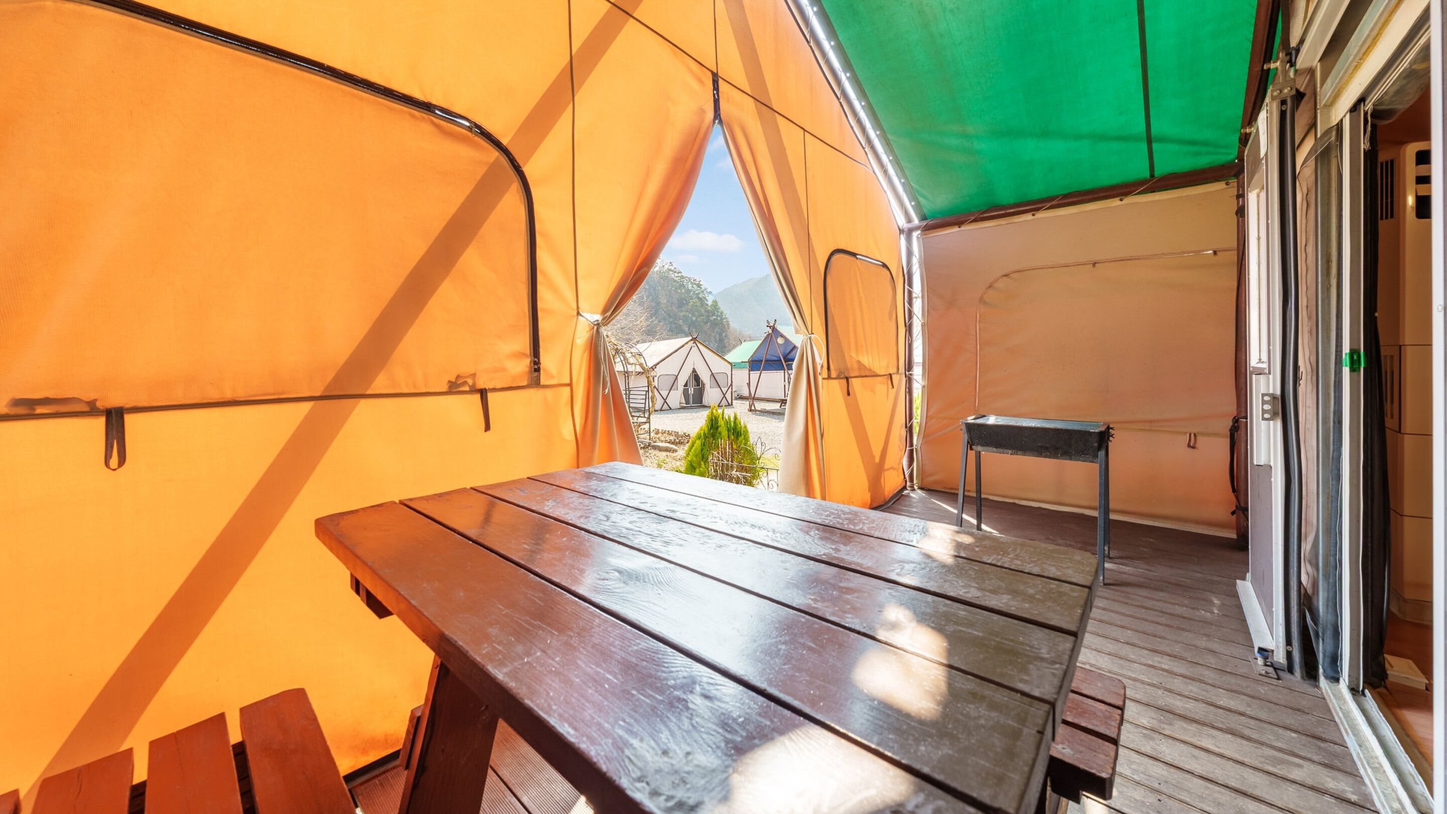 A tent with a wooden table and benches, a ladder, and a small table.