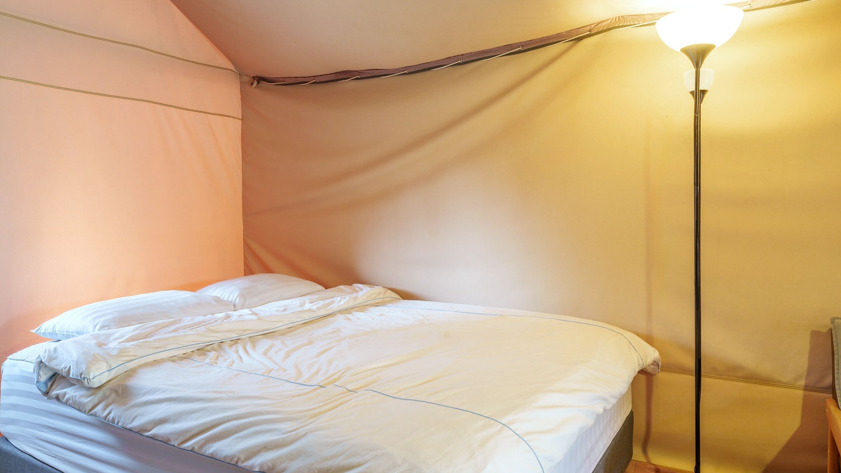 Ein Bett mit weißer Bettwäsche, eine Lampe und eine Wand mit einem Holzbalken.
