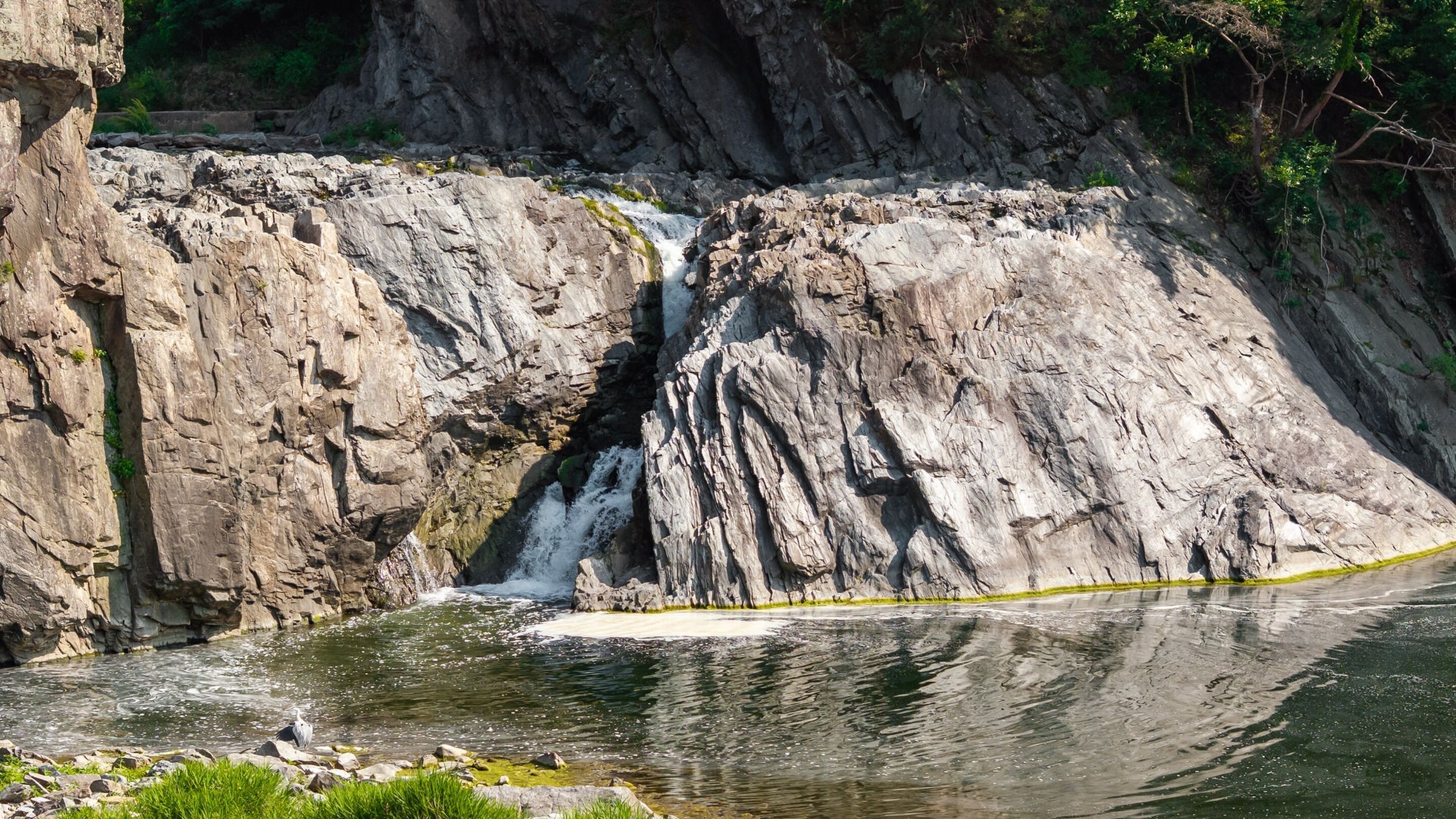 A waterfall cascading down a rocky cliff into a calm river.