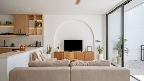 A modern living room with a large sofa, a flat-screen TV, and a kitchen area with wooden cabinets and a marble countertop. - Elements A3 Villa Bingin (Pecatu)