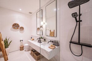 A modern bathroom with a white vanity, two sinks, a large mirror, a shower head, and decorative items on the wall. - Elements A3 Villa Bingin (Pecatu)