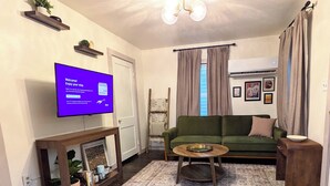 Een woonkamer met een flatscreen-tv waarop een welkomstboodschap staat, een groene bank, een houten salontafel, een tapijt met een patroon en een plafondlamp.