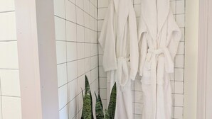 Een badkamer met witte betegelde muren, een zwart-wit geruite vloer en twee witte badjassen hangend aan haken.