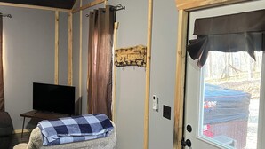 Una habitación acogedora con un sofá gris, un televisor, una puerta de madera con un ventanal y una mesita con una manta.