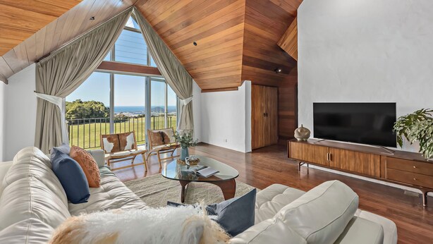 A modern living room with a large TV, wooden ceiling, and a view of the outdoors.