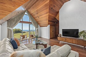 A modern living room with a large TV, wooden ceiling, and a view of the outdoors.