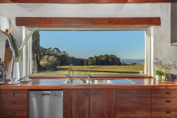 A kitchen with a large window, stainless steel sink, wooden cabinets, and a dishwasher.