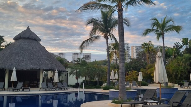 A swimming pool with lounge chairs and umbrellas, surrounded by palm trees and a thatched-roof hut. - Luxury Condo ALAMAR, Riviera Nayarit. Mexico (Cruz de Huanacaxtle)