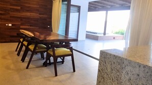 A modern dining area with a wooden table and chairs, a ceiling fan, and a large window with curtains. - Luxury Condo ALAMAR, Riviera Nayarit. Mexico (Cruz de Huanacaxtle)