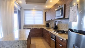 A modern kitchen with granite countertops, stainless steel appliances, and wooden cabinets. - Luxury Condo ALAMAR, Riviera Nayarit. Mexico (Cruz de Huanacaxtle)