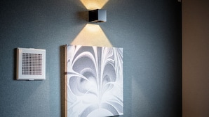 Eine Wandleuchte wirft einen Schatten auf eine strukturierte Wand, ein Rauchmelder und eine Steckdose sind zu sehen.