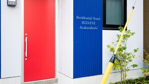 Eine rote Tür mit Griff, eine blaue Wand mit dem Schriftzug "Residential Hotel IKIDANE Asakusabashi" und ein Fenster mit einem gelben Reinigungsstab.
