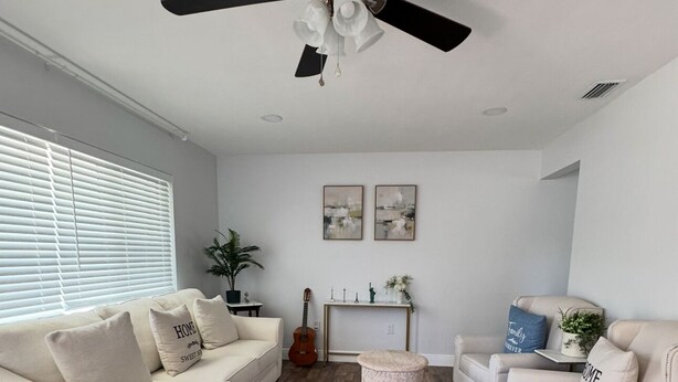 Ein Wohnzimmer mit Deckenventilator, einem weißen Sofa, einem kleinen runden Tisch und Holzboden.