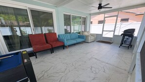 Ein überdachter Patio-Bereich mit einem blauen Sofa, roten Stühlen und einem weißen Sessel.