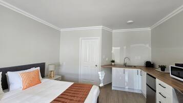 A modern bedroom with a bed, bedside table, lamp, and a kitchen area with cabinets and a sink.