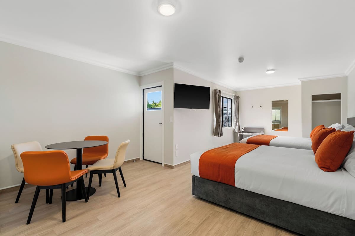 A hotel room with a bed, two chairs, a small table, and a TV.