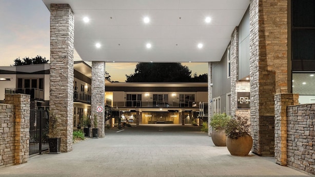 A hotel entrance with stone pillars, a paved driveway, and a sign indicating a 5-minute walk to the hotel. - STAY280 & STAY284 Rotorua (Rotorua)