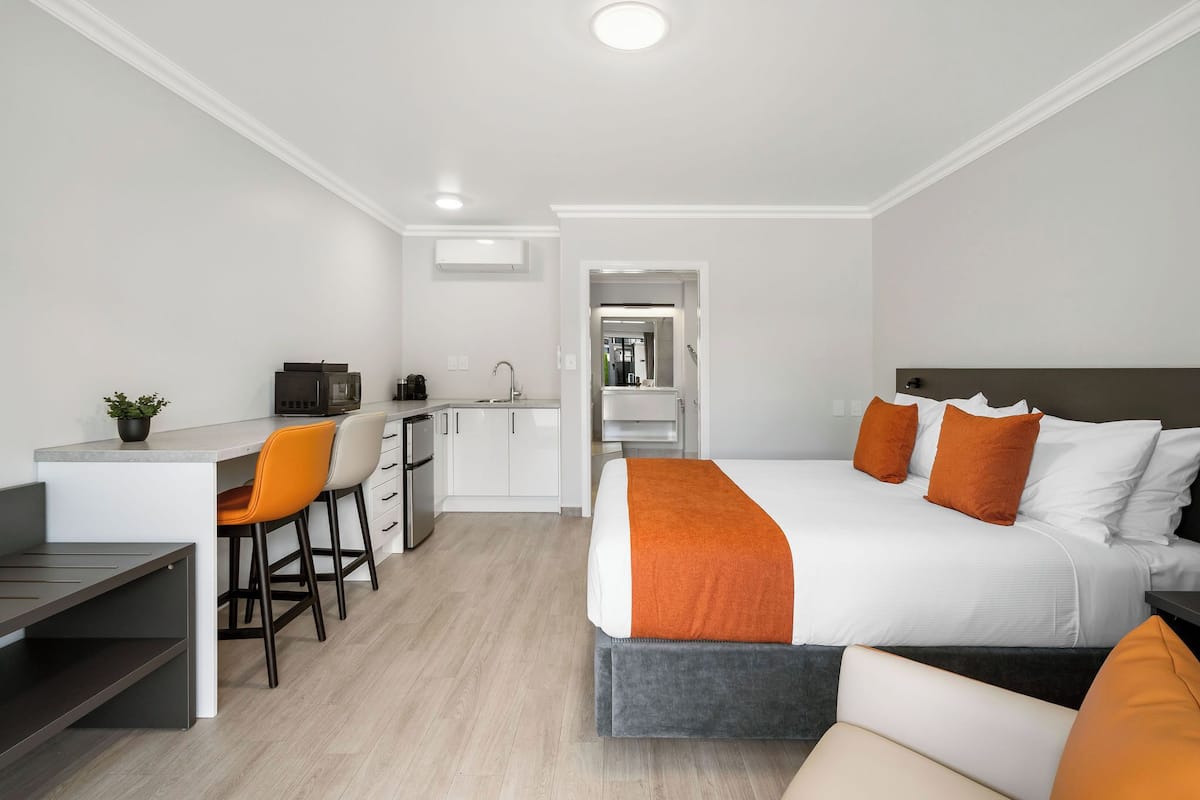 A modern hotel room with a bed, a desk, and a kitchenette.