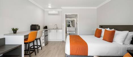A modern hotel room with a bed, a desk, and a kitchenette.