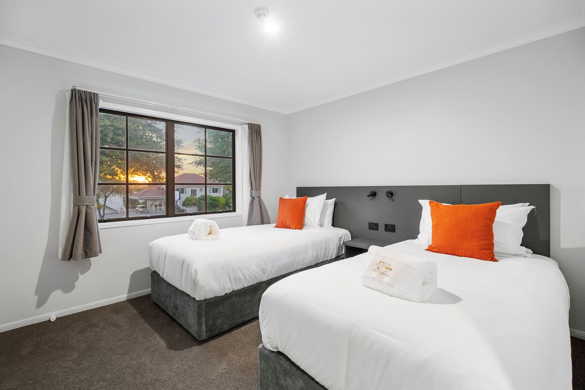 A hotel room with two beds, a large window, and a view of the sunset.