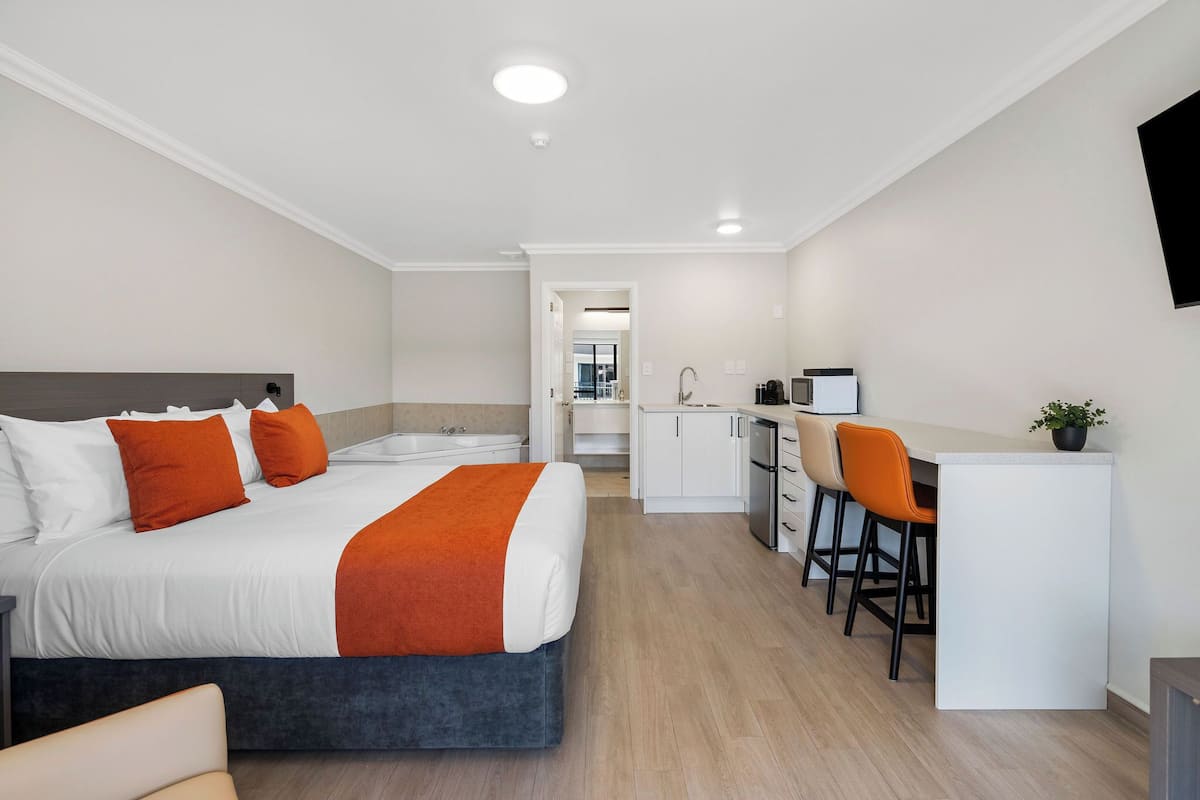 A hotel room with a large bed, a desk, and a kitchenette.