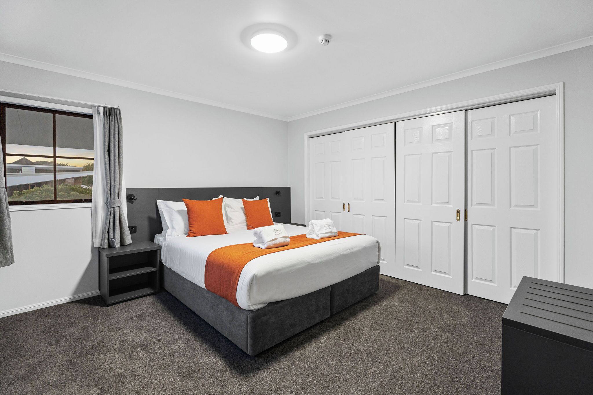 A hotel room with a bed, a nightstand, a wardrobe, and a view of the outside.