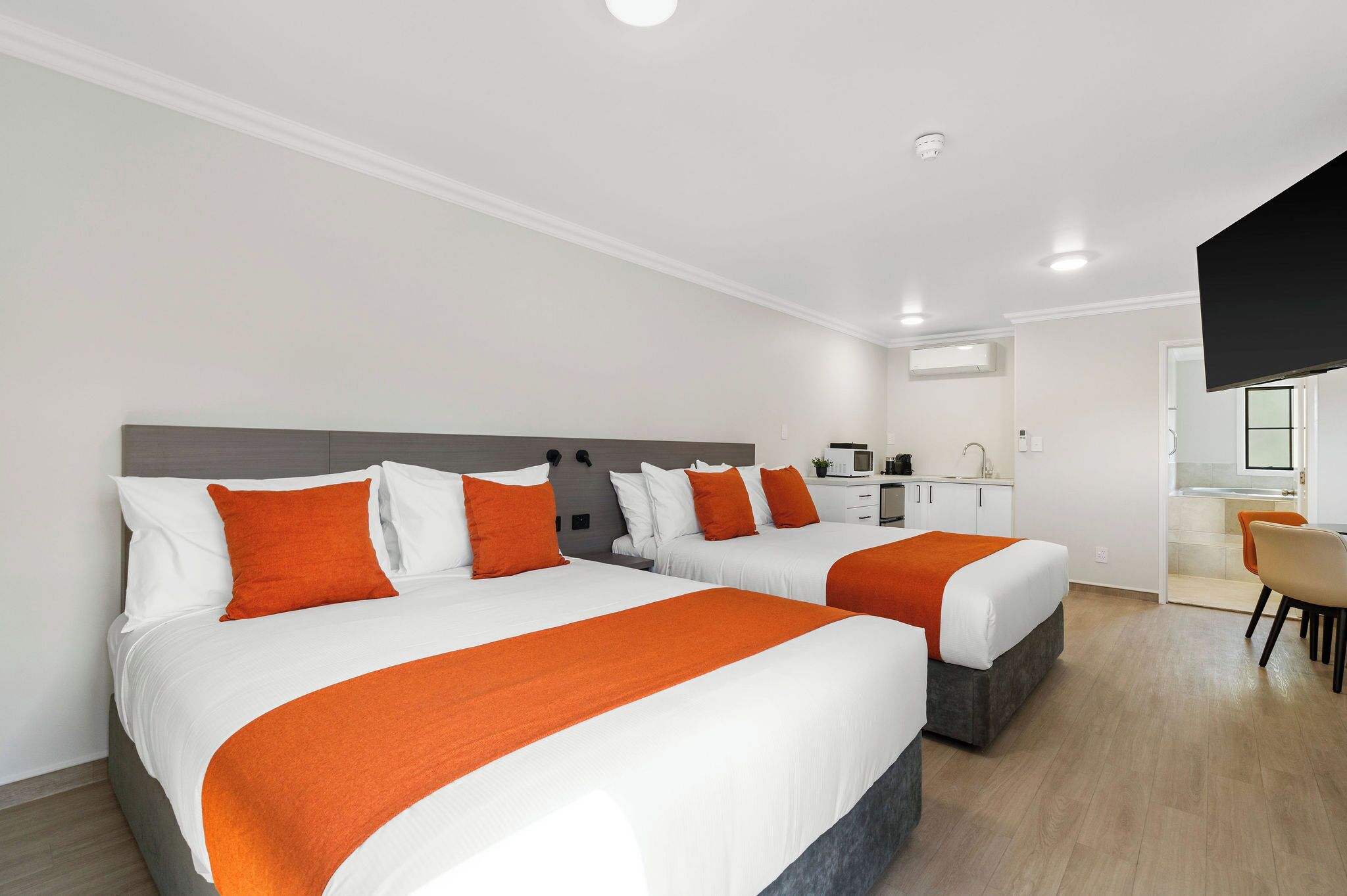 A hotel room with two beds, a desk, a chair, and a kitchenette.