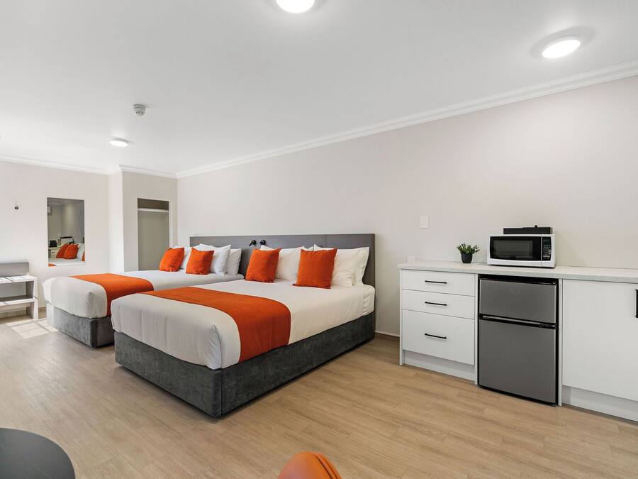 A modern hotel room with a large bed, a desk, a microwave, and a refrigerator.