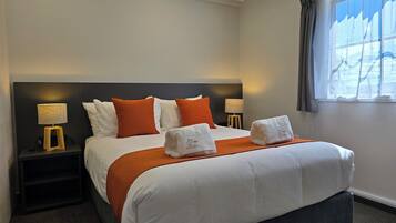 A hotel room with a large bed, two bedside tables, a window with curtains, and a nightstand with a lamp.