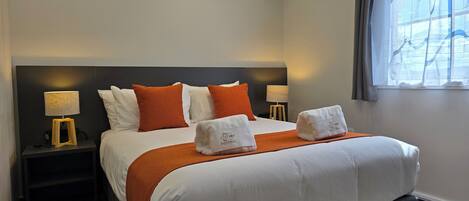 A hotel room with a large bed, two bedside tables, a window with curtains, and a nightstand with a lamp.