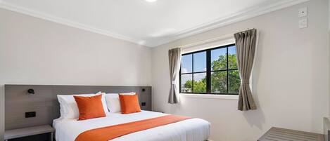 Habitación de hotel moderna con una cama grande, una mesita de noche, calefacción integrada y una ventana con cortinas.