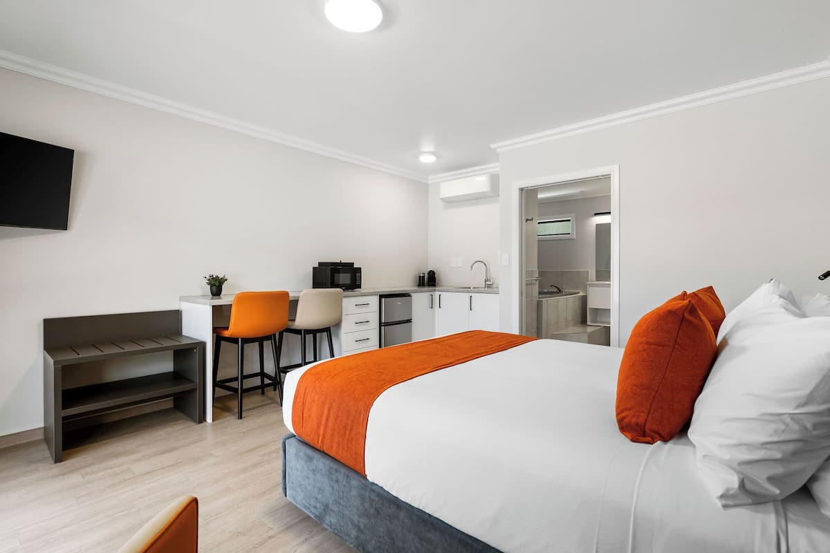A modern hotel room with a bed, a desk, and a kitchenette.