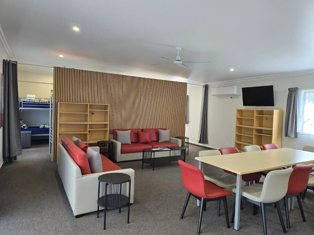 A modern living room with a sofa, a dining table, and chairs. There are bookshelves and a flat-screen TV mounted on the wall.