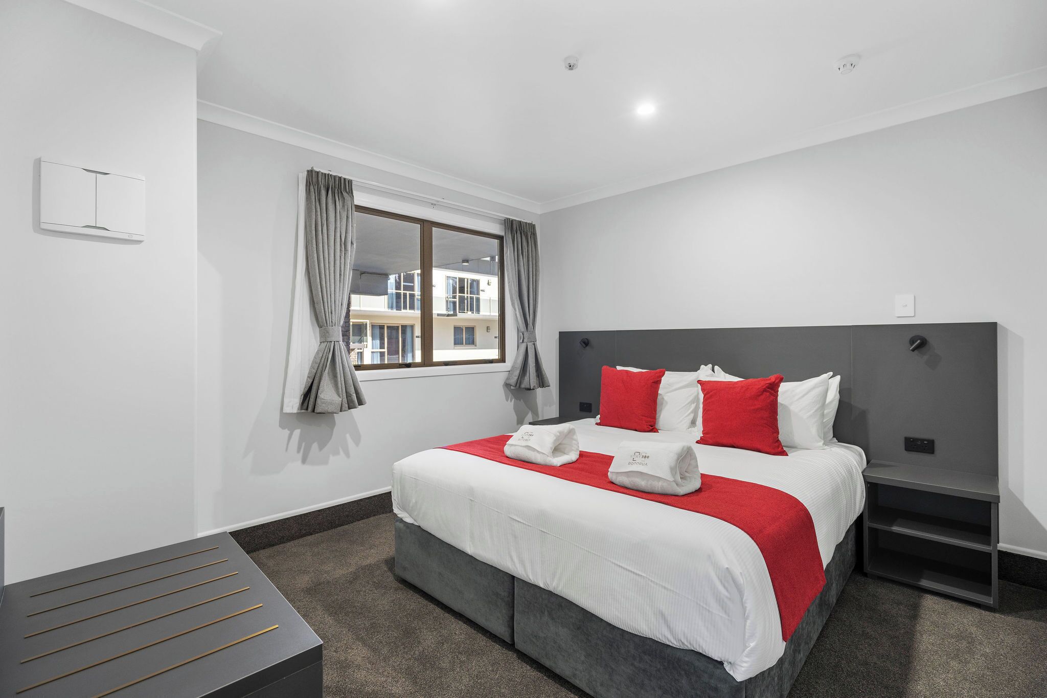 Une chambre d’hôtel moderne avec un grand lit, des rideaux gris, une table de chevet et une vue sur les bâtiments environnants.