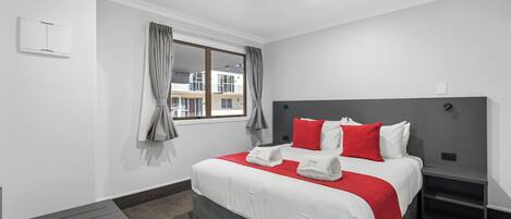 A modern hotel room with a large bed, grey curtains, a bedside table, and a view of buildings outside.