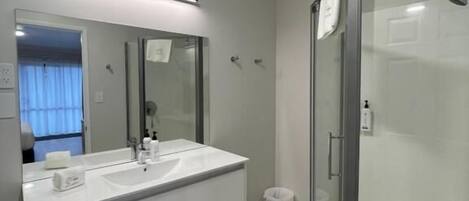 A modern bathroom with a large mirror, two sinks, a shower, and a glass-enclosed shower area.