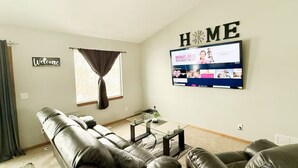 A living room with a leather sofa, a coffee table, and a TV mounted on the wall displaying a show.
