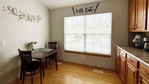 A dining area with a table and chairs, a window with blinds, and wooden cabinets.