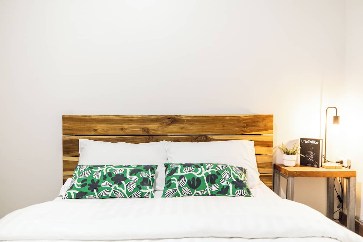 A bed with a wooden headboard, white bedding, and two green pillows with a floral pattern.