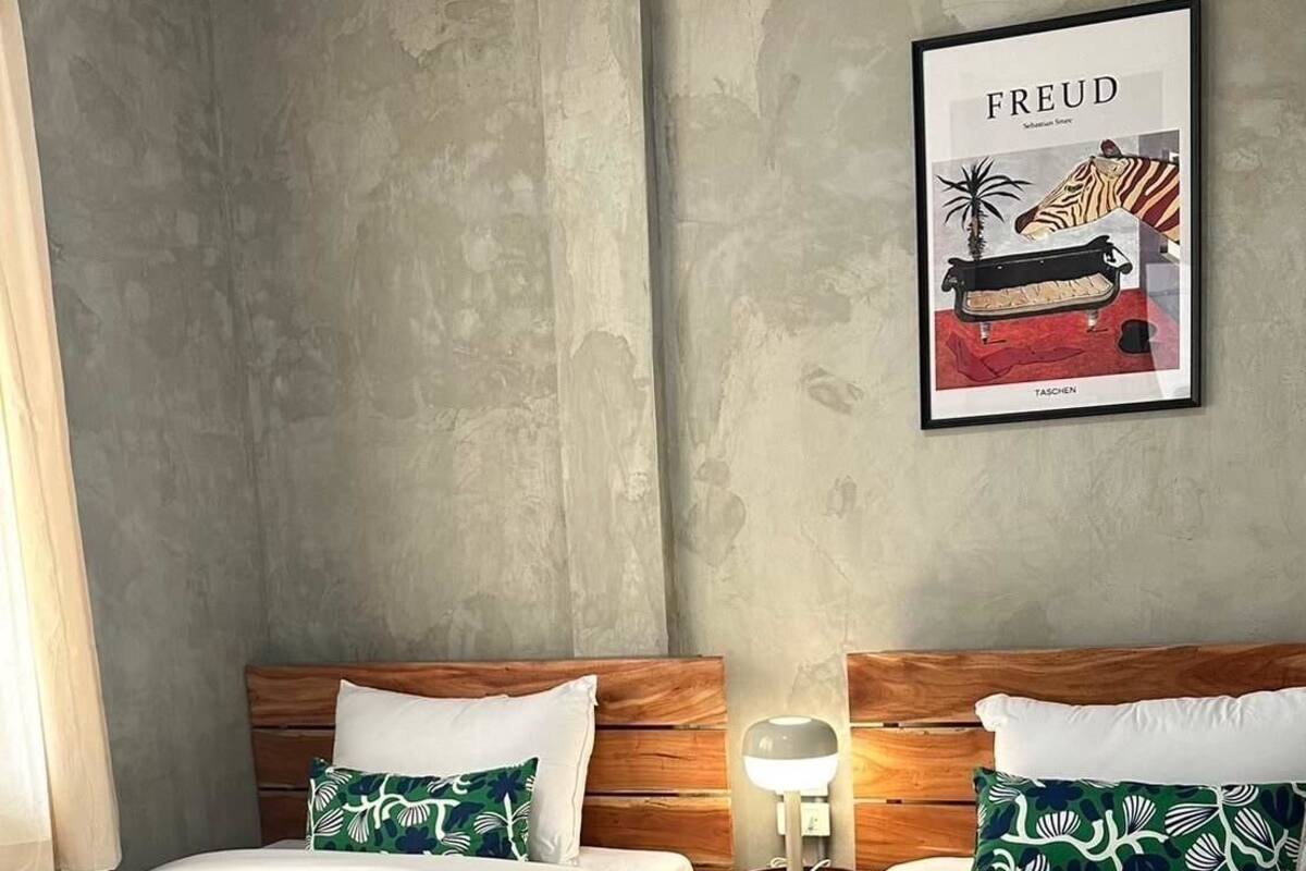A hotel room with two beds, each with white bedding and green patterned pillows. There is a framed picture on the wall above the beds.