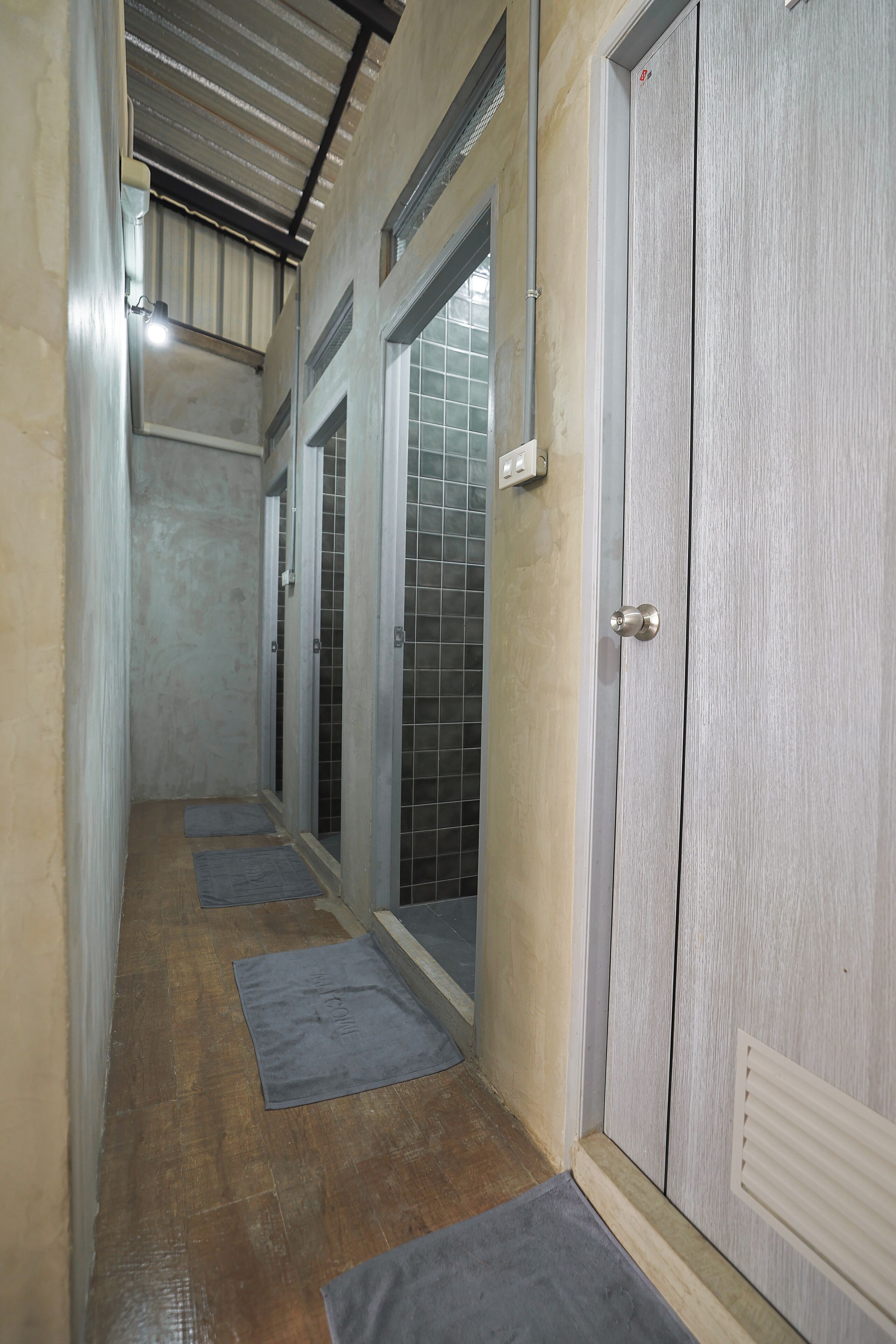 A narrow hallway with a wooden floor, grey mats, and a door with a metal handle.
