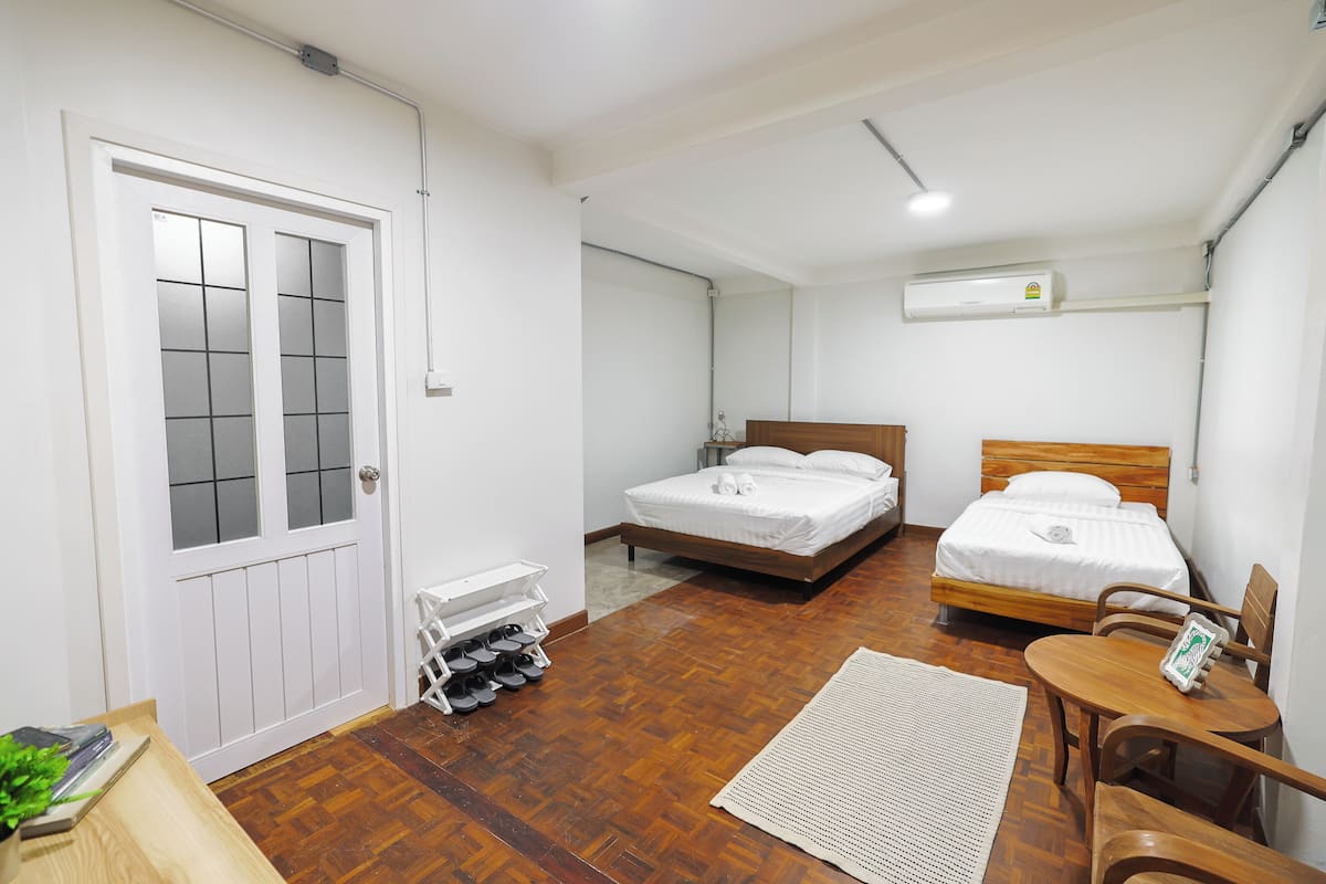 A bedroom with two beds, a wooden floor, a white door, and a shoe rack.